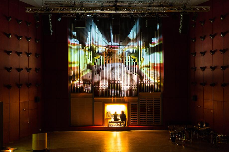Blick aus der Konzertsaalmitte auf die illuminierte Orgel. Am Orgeltisch muszieren die Professoren Jürgen Essl und Helmut Deutsch.