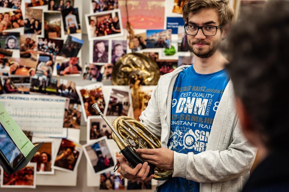Hornstudent im Dialog mit seinem Lehrer. Im Hintergrund mit Bildern verzierte Soundpanele.