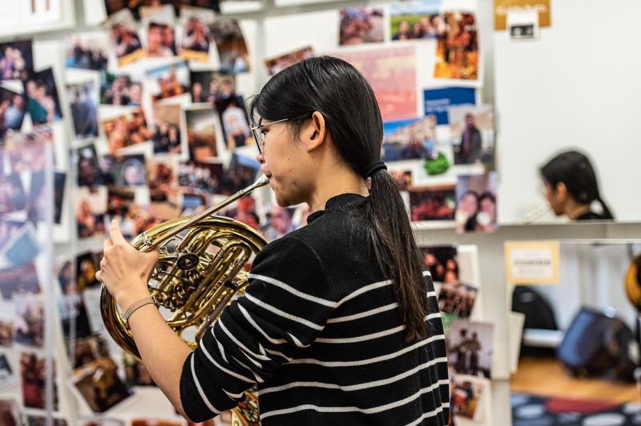Hornstudierende in einer Unterrichtssituation. Im Hintergrund sieht man die unterschiedlichen gestalteten Soundpanele, die Studierende und Alumni der letzten Jahrezeigen.