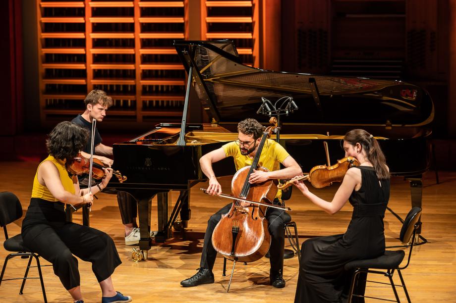 Musizierendes Klavierquartett auf dem Konzertsaalpodium.