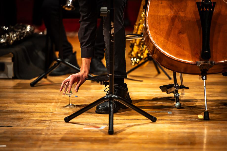 Kontrbassist taucht mit einem Finger in ein mit Wasser gefülltes Weinglas.