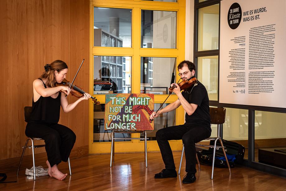 Violinstudierende beim Musizieren in der Wandelhalle. Im Hintergrund ist die Bibliothek zu erkennen.