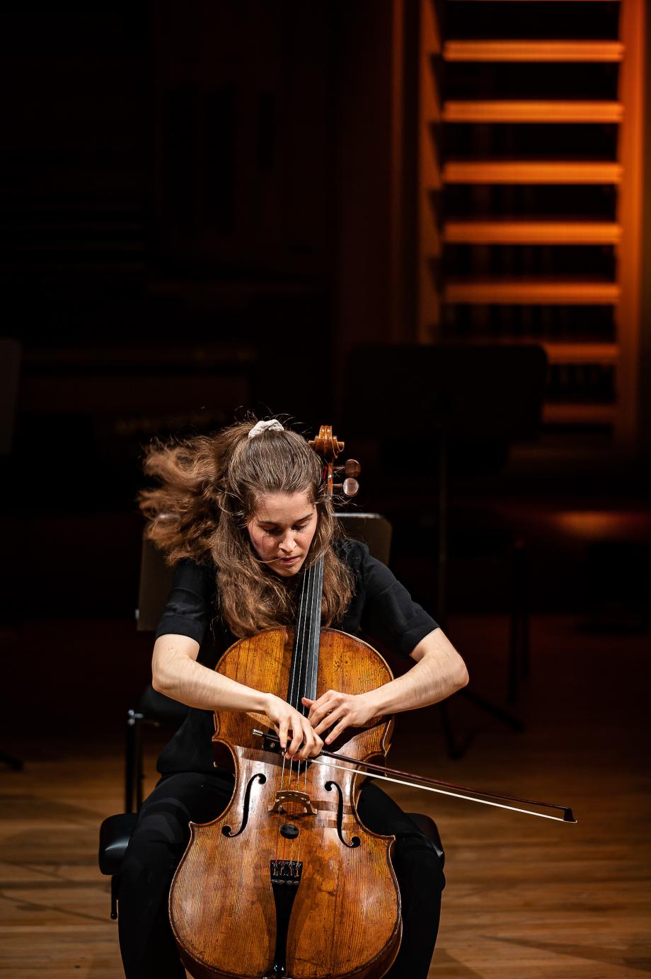 Die Cellistin Nicola Pfeffer beim bewegenden Spiel. Durch das Spiel sind die langen Haare in Bewegung. Der Blick liegt auf dem Griffbrett und ihren Händen.