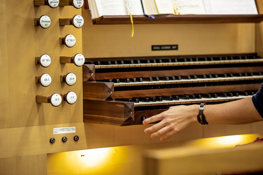 Detailaufnahme der dreimanualigen tastutur der Gollorgel. Die Hand einer Studierenden wendet sich einem Schaltknopf auf der linken Seite zu.