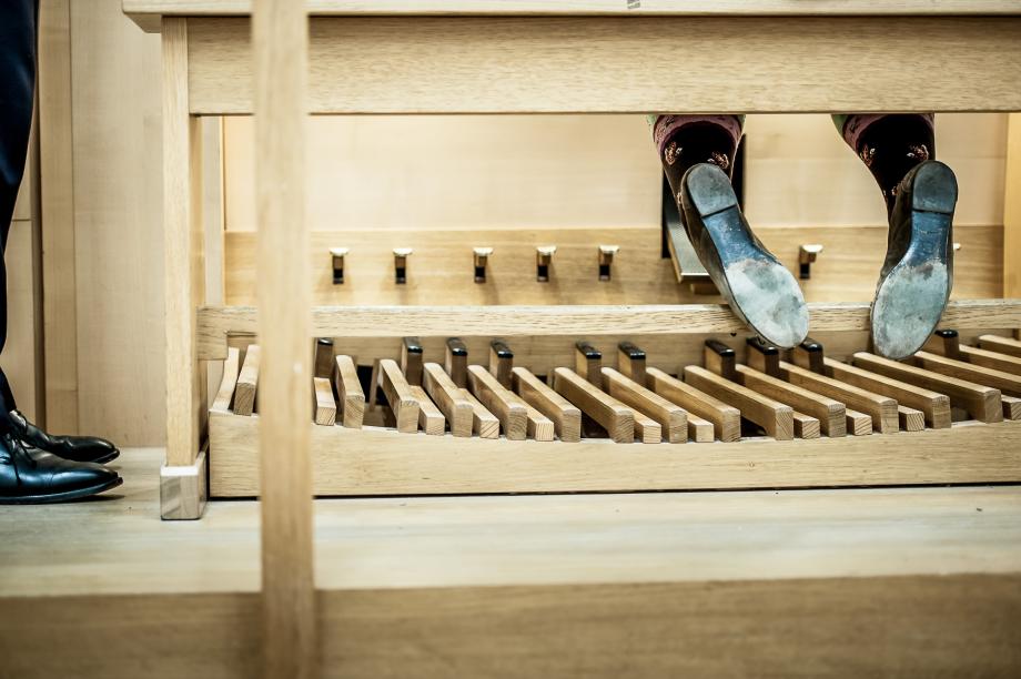 Detailaufnahme der Orgelbank und der Fußpedale. Die Füße der Organistin sind hinter der Holzverstrebung eingehängt. Die Sohle der Orgelschuhe ist sehr abgewetzt.