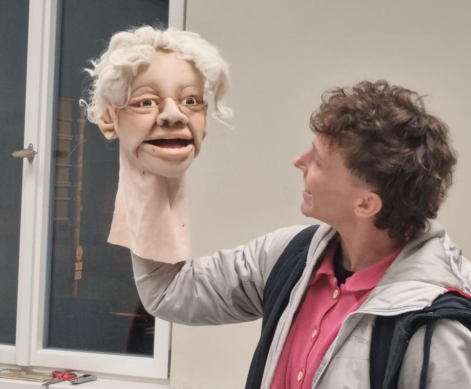 Student*in schaut lachend einen Figurenkopf, den sie in der Hand hält, an.