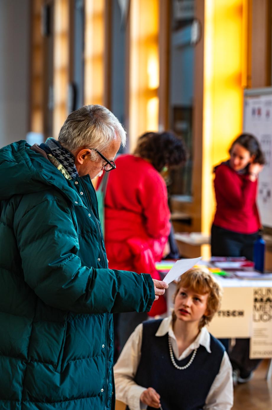 Studentische Teilnehmende in der Wandelhalle beim Infotisch im Gespräch.